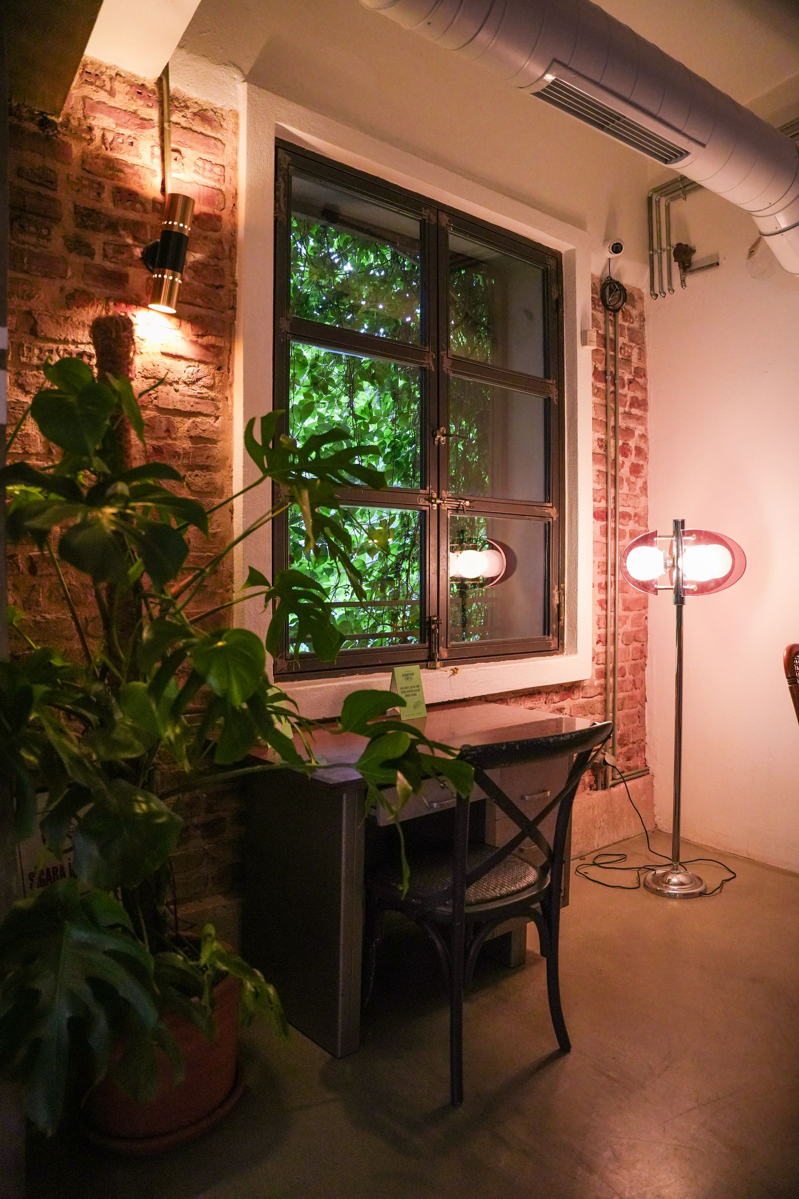 Warm interior of a loft with brick walls, a desk, plants, and soft lighting.