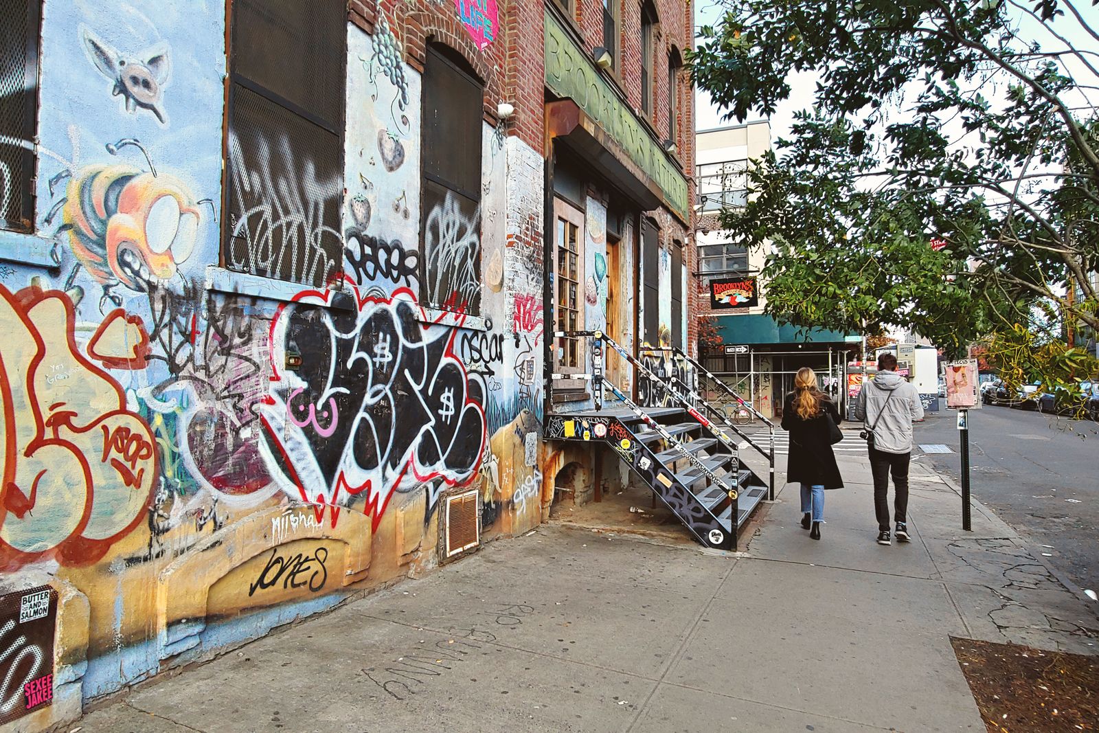 Colorful graffiti in a Brooklyn alley with two people walking, capturing urban street art.